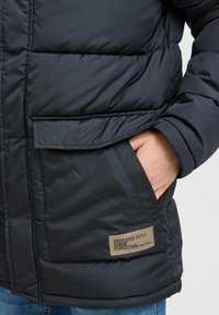 Chaqueta puffer de color azul oscuro con un acabado texturizado, que cuenta con un bolsillo delantero y una etiqueta que dice "DEDICADO A LA PERFECCIÓN DEL DENIM".