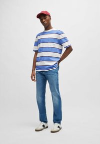 Camiseta de rayas azul y blanca de manga corta con un bolsillo en el pecho, combinada con jeans azul claro y zapatillas blancas con detalles en negro. Gorra roja.