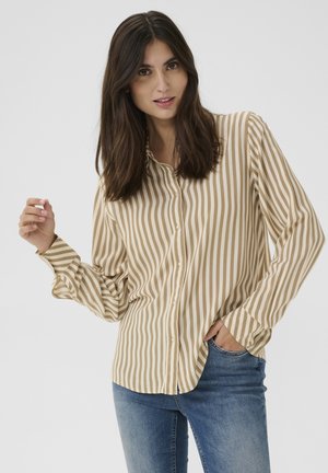 Camicia a righe beige e crema con colletto classico e maniche lunghe, abbinata a jeans blu, che mostra una vestibilità rilassata e una texture morbida.