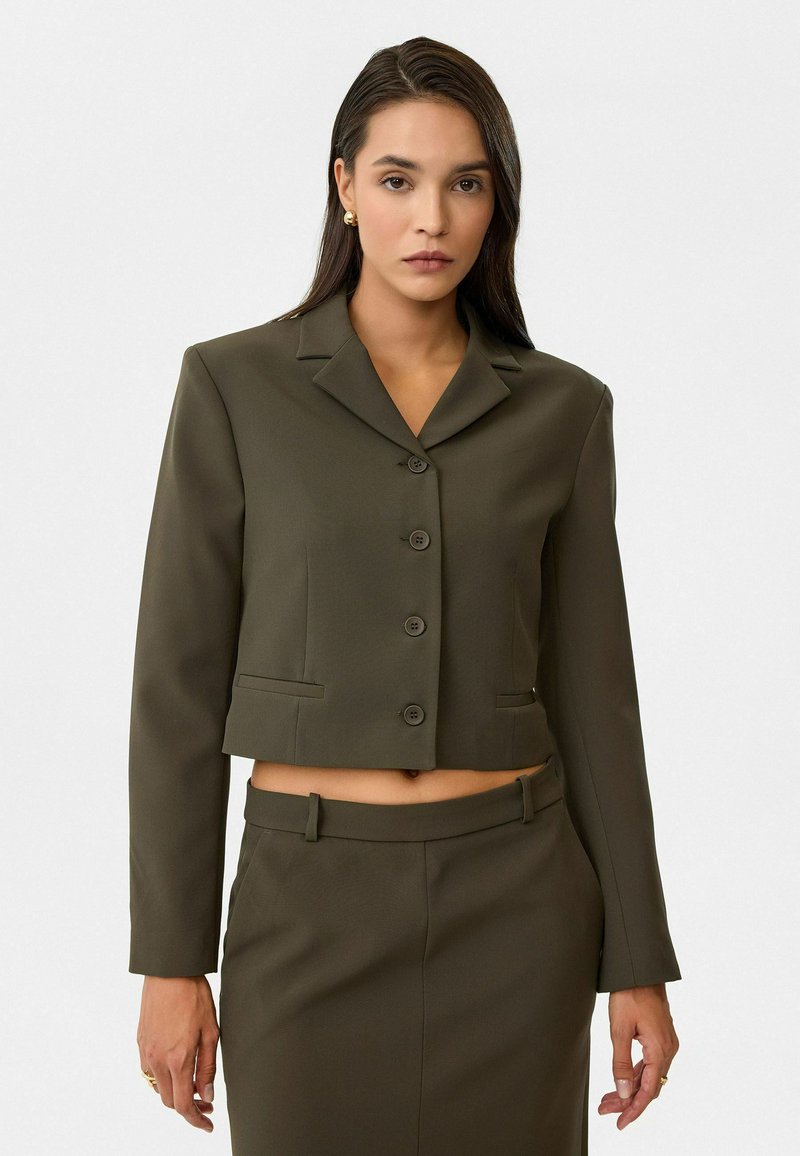 Veste blazer cropped en vert olive avec un col cranté, cinq boutons et deux poches avant. Texture lisse et coupe ajustée.