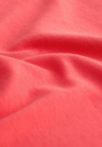 Gros plan sur un tissu rose corail lisse avec des plis doux et une texture tissée visible.