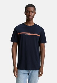 Mørkeblå bomulds T-shirt med et trykt rød-orange stribe og teksten "DENIM EST. 2007." Kortærmet og med rund halsudskæring, løs pasform.