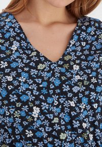 Top z materiału w kwiatowy wzór, z dekoltem w kształcie litery V, w dominującej czarnej kolorystyce z niebieskimi, białymi i zielonymi kwiatami. Miękka struktura, lekki.