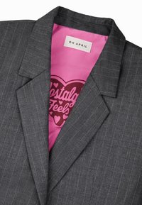 Harmaaraidallinen bleiseri, jossa on kaulus, pinkki satiinivuori ja sisällä graafinen printti, jossa lukee "Nostalgisia tunteita".