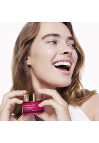 Różowy słoik kremu Merveillance LIFT z złotą pokrywką, trzymany przez osobę. Gładka powierzchnia, oznakowany jako środek do korekcji zmarszczek i ujędrniania.