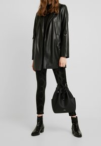 Blazer de cuero negro con mangas largas y correas laterales, combinado con leggings negros con estampado de serpiente texturizado, y complementado con botas negras hasta el tobillo y un bolso tipo cubo.