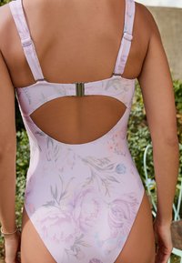 Enfärgad baddräkt i pastellrosa med blommönster, justerbara axelband och öppen ryggdesign. Utrustad med en metallklämma för säker stängning.