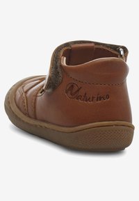 Brun läderankelstövlett med en texturerad baksida, mjuka tygdetaljer och en gummisula. Har en logotyp på sidan och kontrasterande sömmar.