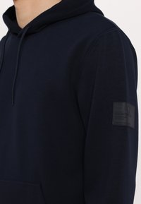 Felpa blu navy realizzata in tessuto morbido, con tasca a marsupio e un'etichetta logo testurizzata sul manica sinistra.