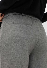 Pantaloni della tuta grigi con una texture morbida, dotati di una vita arricciata e una singola tasca posteriore. Hanno un design a gamba dritta.