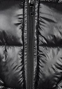 Schwarze Pufferjacke mit einem zentralen Reißverschluss. Glatte, glänzende Außenseite mit gesteppten Nähten und einer gepolsterten Konstruktion zur Isolierung.