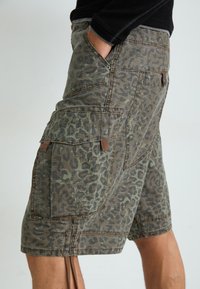 Cargo-Shorts im grünen und braunen Leopardenmuster, aus leichtem Stoff, mit mehreren Taschen und Kordelzugdetails.