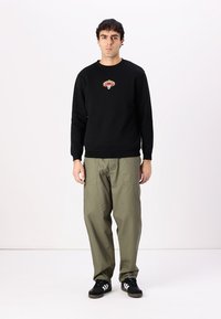 Black sweatshirt with round neckline and embroidered design, paired with loose olive green pants and black sneakers.