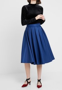 Musta pitkähihainen poolopaita yhdistettynä farkkukankaisiin sinisiin midihameisiin. Jalkineissa on punainen leopardikuosi ja mustat hihnavaihtoehdot.