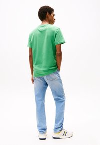 Green cotton t-shirt with short sleeves, paired with light blue denim jeans. The t-shirt has a crew neckline and a relaxed fit.