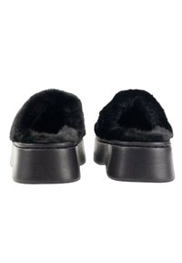 Zapatos negros de pelo sintético sin cordones con una suela plana y gruesa en negro. El interior es suave, proporcionando comodidad y calidez. Textura suave en todo.