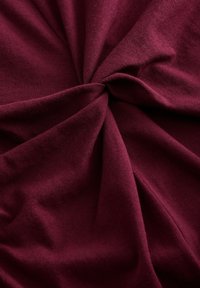 Tissu bordeaux avec une texture douce et lisse, présentant un design torsadé avec des plis drapés et un motif côtelé subtil.