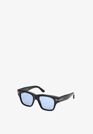 Gafas de sol rectangulares negras con lentes azul claro y logo blanco en forma de T en las patillas, posicionadas en ángulo sobre fondo blanco.