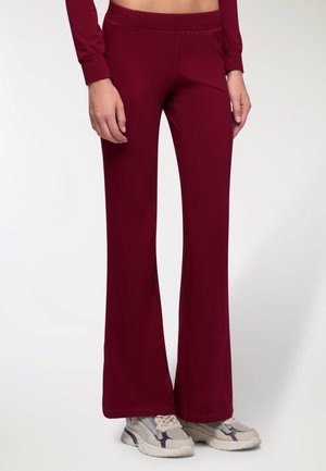 Pantaloni a palazzo bordeaux realizzati in tessuto morbido con una fascia in vita elastica, abbinati a sneaker grigie chiare con suola testurizzata.