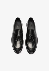 Mocassins en cuir noir avec une finition lisse, dotés d'un détail en pampille et d'un bout arrondi. Le design comprend des accents de couture subtils.