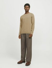 Jasnobrązowy sweter dzianinowy z długimi rękawami w zestawieniu z szarymi, luźnymi spodniami i brązowymi butami na grubej podeszwie. Prosty design, bez widocznych wzorów.