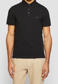 Polo noir en coton avec un col classique et une patte de boutonnage à trois boutons. Il dispose de manches courtes et d'un petit logo sur la poitrine.