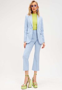 Completo in tessuto a quadri blu e bianco con giacca su misura e pantaloni a zampa, abbinato a un top verde a coste e tacchi alti verdi.