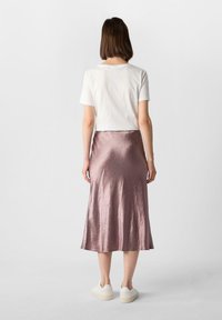 Biała koszulka z krótkim rękawem zestawiona z lekko różową, satynową spódnicą, sięgającą do połowy łydki, noszoną z białymi trampkami.
