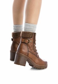 Botas de tobillo de cuero marrón con un puño de punto texturizado, cordones en la parte delantera, cremallera lateral y un tacón apilado. Presentan un acento estampado en el lateral.