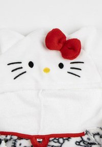 White plush hoodie with cat-shaped hood, featuring black whiskers, a yellow nose, and a red bow accent. Texture is soft and fuzzy.