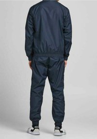 Marinsjöblå träningsdräkt i lätt material, med elastiska muddar och midja. Baksidan visar en slät och elegant design.