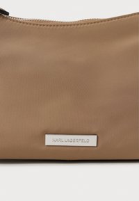 Hnedá nylonová taška s hladkým povrchom, striebornými detailami a vyvýšeným logom "KARL LAGERFELD". Zips na hornej hrane. Kompaktný dizajn.