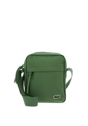 Green compact crossbody bag with front zipper pocket, adjustable strap, and small crocodile logo on bottom right corner.