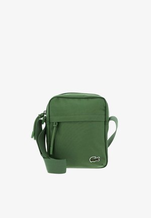 Green compact crossbody bag with front zipper pocket, adjustable strap, and small crocodile logo on bottom right corner.