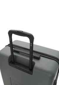 Gray hard-shell suitcase with a black telescopic handle and push-button mechanism, featuring a zipper and textured surface.