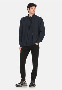 Navy bomber jacket with a front zipper, ribbed cuffs, and hem. Paired with black pants and gray-black sneakers. Smooth fabric finish.