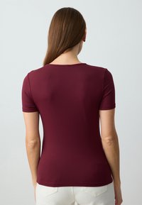 Bordowy top z krótkim rękawem i okrągłym dekoltem, wykonany z gładkiego, elastycznego materiału. Posiada dopasowany krój i subtelną fakturę.