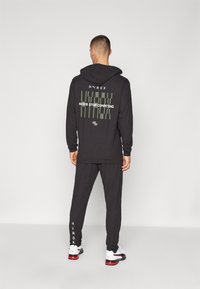 Svart hoodie med text på baksidan, ihop med matchande svarta byxor. Har gröna och vita grafiska tryck, en bekväm passform och sportskor.