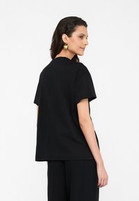 T-shirt nera in cotone con vestibilità rilassata, maniche corte e collo a giro; presenta una texture liscia e un design semplice.