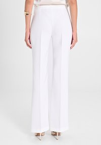 Pantaloni bianchi a gamba larga con una vestibilità liscia e su misura. Presentano un'alta vita e cuciture verticali, abbinati a scarpe con tacco alto color nude.