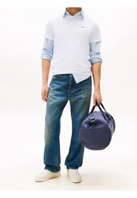 White T-shirt layered over a blue striped shirt, paired with blue jeans and white sneakers. A navy duffel bag is held in one hand.