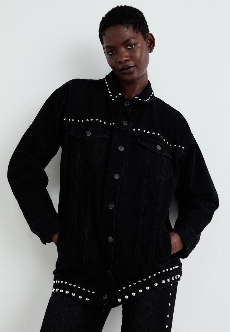 Black denim jacket with silver studs along the collar and hem. Features button closure, two front pockets, and a relaxed fit.