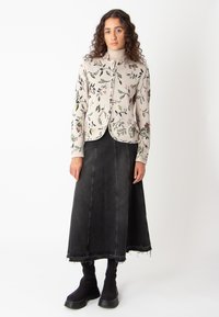 Kootud kardigan helesbeiges värvuses lilleline tikandiga; koos tume denimpükste A-joone seelikuga ja mustade ribakujuliste pahkluuslatega.