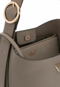 Sac à main en cuir synthétique gris avec un détail circulaire en métal doré et une poche intérieure zippée. Présente un logo en relief.