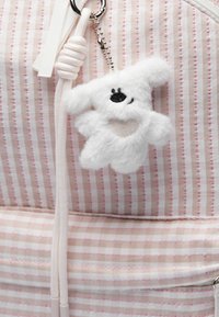 Striped fabric backpack in pink and white with a fuzzy white bear keychain featuring black facial details and a heart-shaped patch.