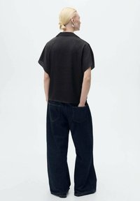 Sort kortærmet skjorte med krave, parret med løstsiddende mørk denimjeans med baglommer og en afslappet silhuet.