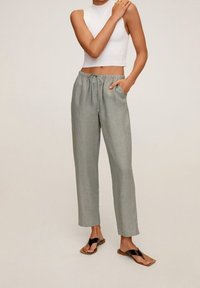 Lichtgroene linnen broek met een losse pasvorm, elastische tailleband en zijzakken, gecombineerd met een wit mouwloos topje en zwarte slippers.