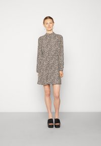 Vestido com padrão de leopardo, mangas longas, gola alta e uma silhueta fluida. Usado com sandálias de plataforma pretas.