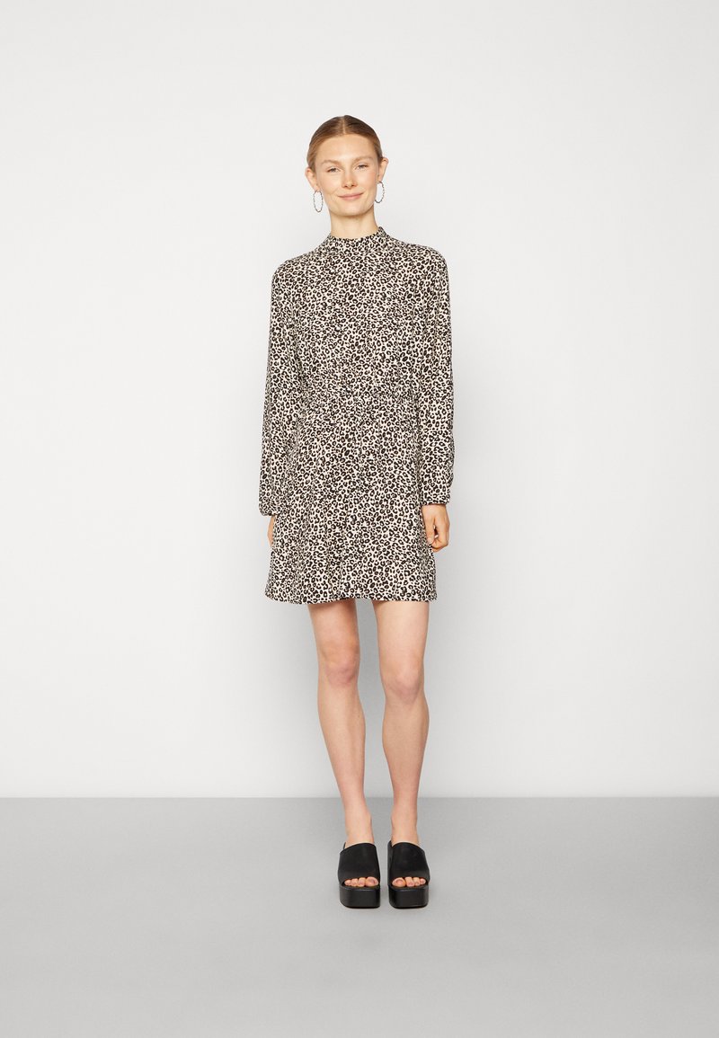 Vestido com padrão de leopardo, mangas longas, gola alta e uma silhueta fluida. Usado com sandálias de plataforma pretas.