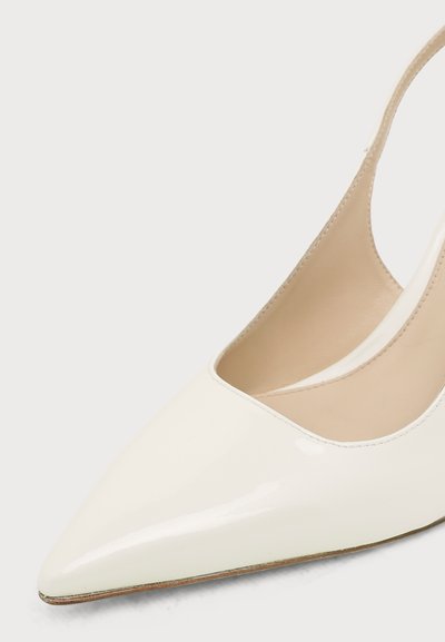 Chaussure slingback en cuir verni blanc à bout pointu avec doublure intérieure beige et petit talon sur un fond clair uni.